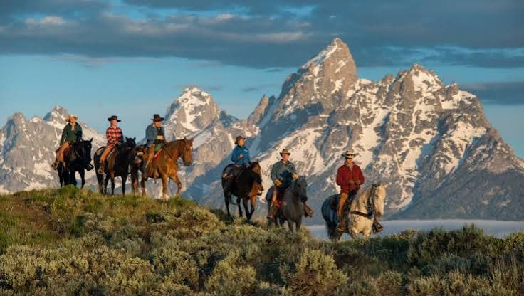 Horseback riders with the Grand Tetons rising behind them at sunrise