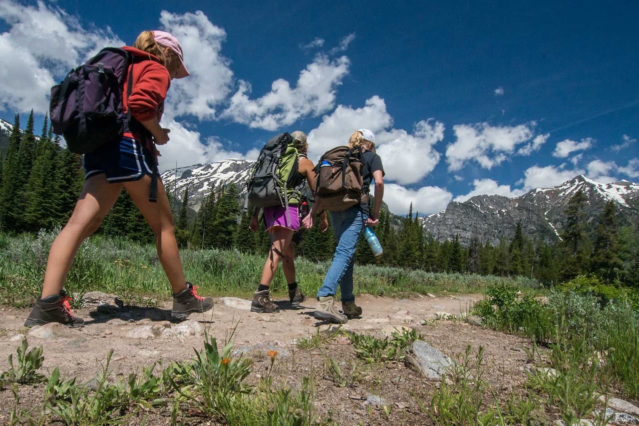 Hikers on an alpine trail below snow-capped Teton peaks