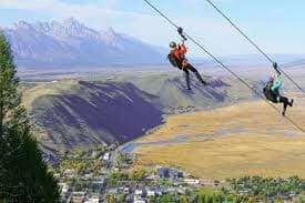 Twin zipline riders above Jackson Hole with Teton views